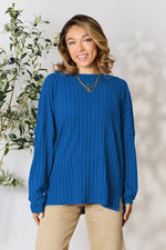 Woman wearing a blue ribbed knit long sleeve top paired with beige pants and layered necklaces