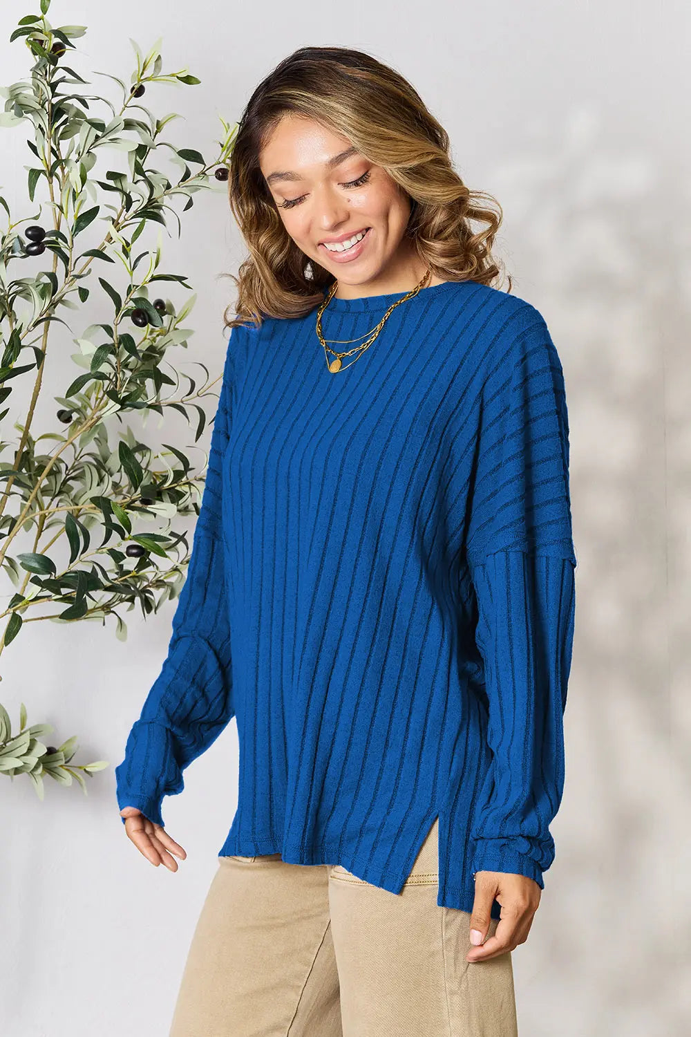 Woman wearing a blue ribbed knit long sleeve top with side slits and beige pants