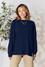 Woman wearing navy blue ribbed knit long sleeve sweater with beige pants standing indoors