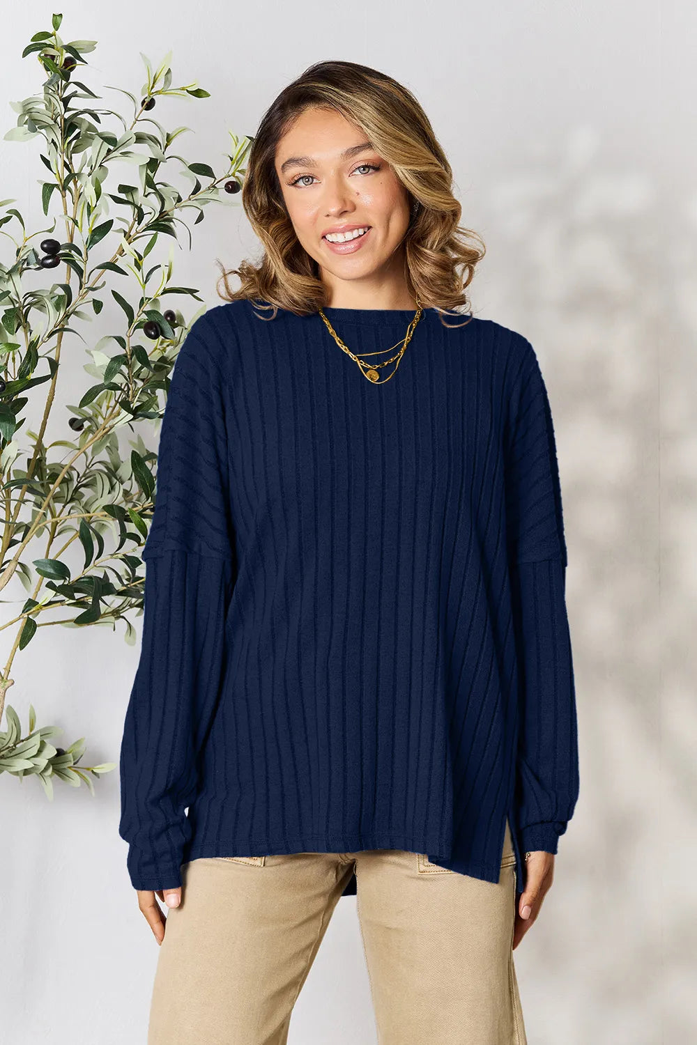 Woman wearing navy blue ribbed knit long sleeve sweater with beige pants standing indoors