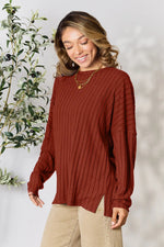 Woman wearing a rust-colored ribbed knit long sleeve sweater with side slits and beige pants