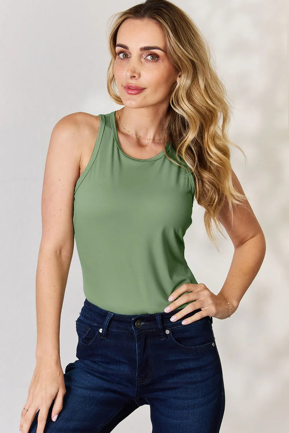 Woman wearing olive green sleeveless top tank tops paired with dark blue jeans