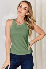 Woman wearing a green sleeveless top tank tops paired with dark blue jeans against a neutral background